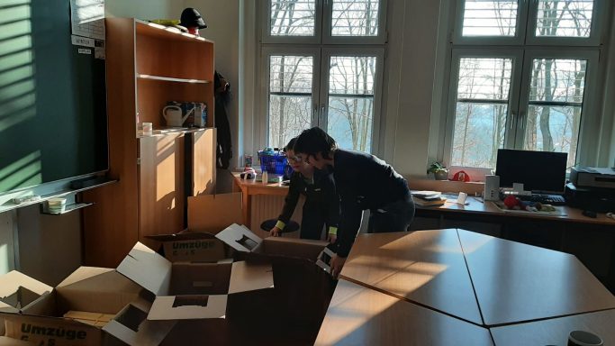 Ein Mann arbeitet an einem Tisch in einem hellen Büro mit Fenstern.