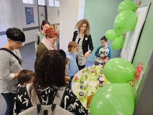 Gruppierung von Personen, die an einem Tisch mit grünen Ballons und Ausstellungsmaterial stehen.