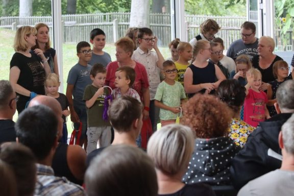Kinder und Erwachsene stehen gemeinsam auf einer Bühne während einer Aufführung.