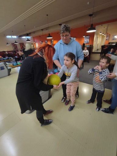Eine Gruppe von Kindern und Erwachsenen in einem Bowlingcenter mit einer Bowlingkugel.