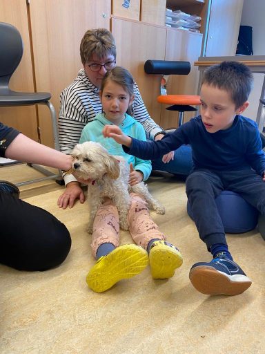 Eine Frau sitzt auf dem Boden mit zwei Kindern und einem kleinen Hund.