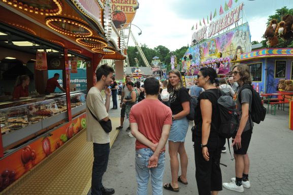 Gruppe von Menschen steht in einem Vergnügungspark vor einem Essensstand.
