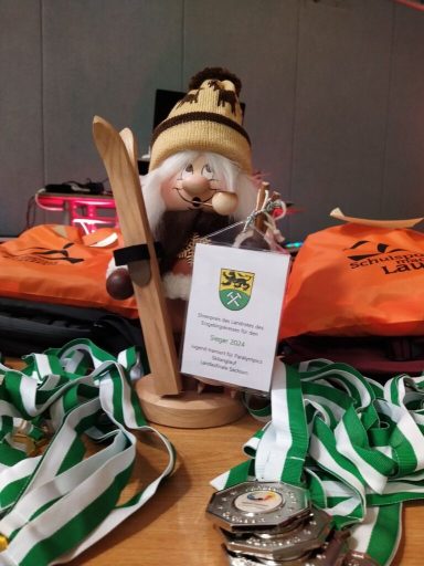 Ein Skifahrer-Dekofigur mit Medaillen und orangefarbenen Taschen im Hintergrund.