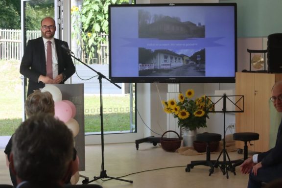 Mann am Rednerpult mit Präsentation und Sonnenblumen im Hintergrund.