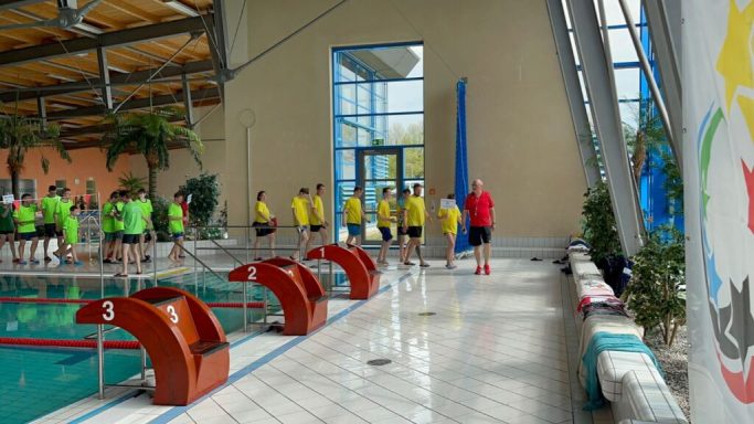 Gruppentraining im Schwimmbad mit Teilnehmern in gelben T-Shirts.