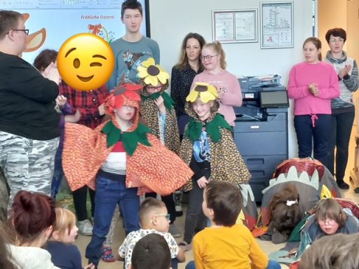 Kinder in Kostümen mit Blumen und Tieren bei einer Bühnenaufführung in einer Gruppe.