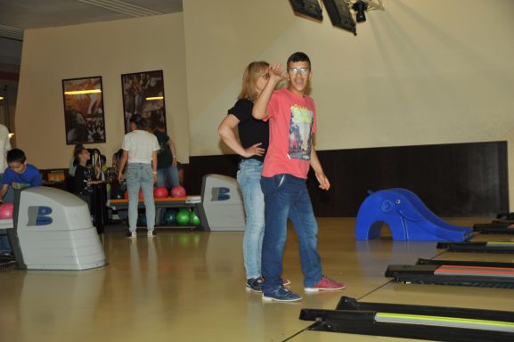 Zwei Jugendliche stehen in einer Spielhalle, im Hintergrund sind weitere Besucher und Spielgeräte.