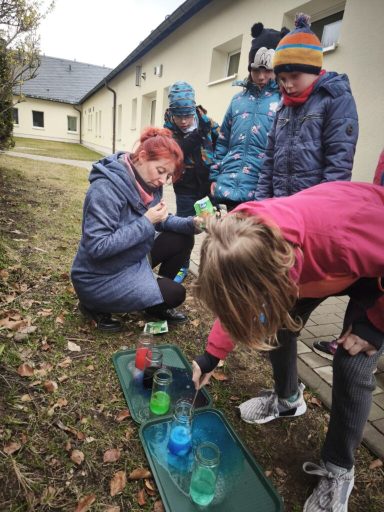 Kinder experimentieren mit bunten Flüssigkeiten im Freien unter Anleitung.