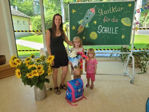 Frau mit zwei Kindern, Sonnenblumen und einer Schultafel im Hintergrund.