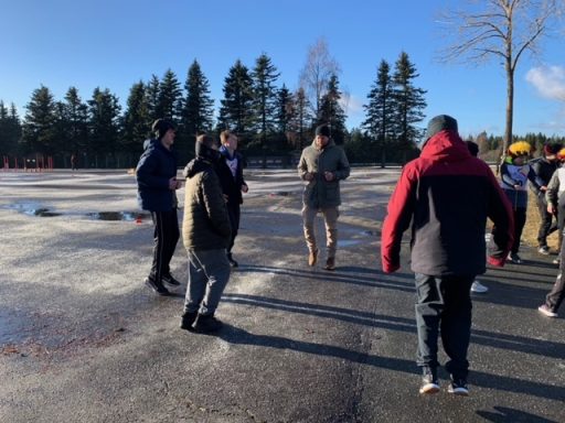 Gruppe von Menschen steht im Freien auf einem Parkplatz, umgeben von Bäumen.