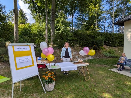 Frau mit Luftballons steht an einem Tisch in einem Garten mit Pflanzen.