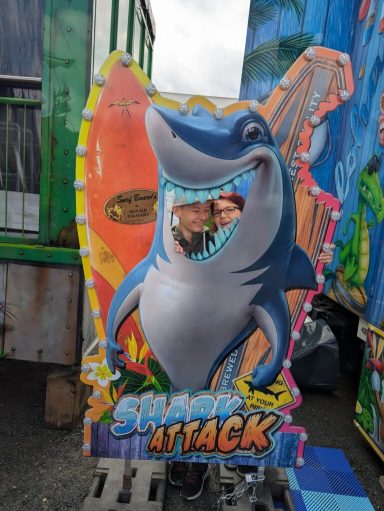Buntes Schild mit einem Hai, der lächelt und einen Menschen im Mund hat, umgeben von Entourage.