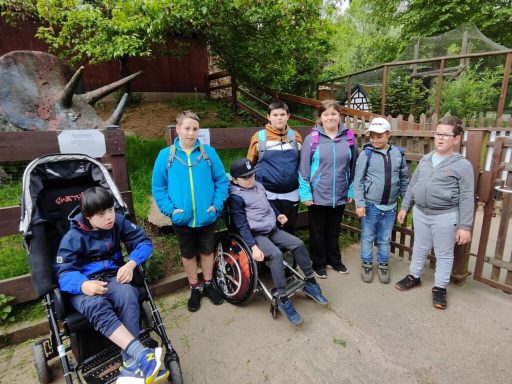 Gruppenschüler mit Behinderungen stehen lächelnd neben einem Zaun im Freigelände.