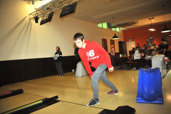 Junge in rotem Sweatshirt beim Bowling in einer geselligen Umgebung.