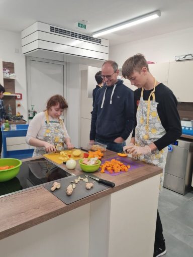 Drei Personen in einer Küche schneiden Gemüse und bereiten Mahlzeiten vor.