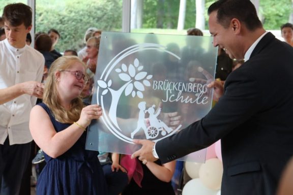 Eine lächelnde Person in einem blauen Kleid erhält eine dekorative Platte von einem Mann.