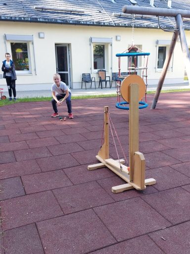 Ein Kind spielt mit einem Holzspielzeug auf einem Spielplatz mit Wippe und anderen Geräten.