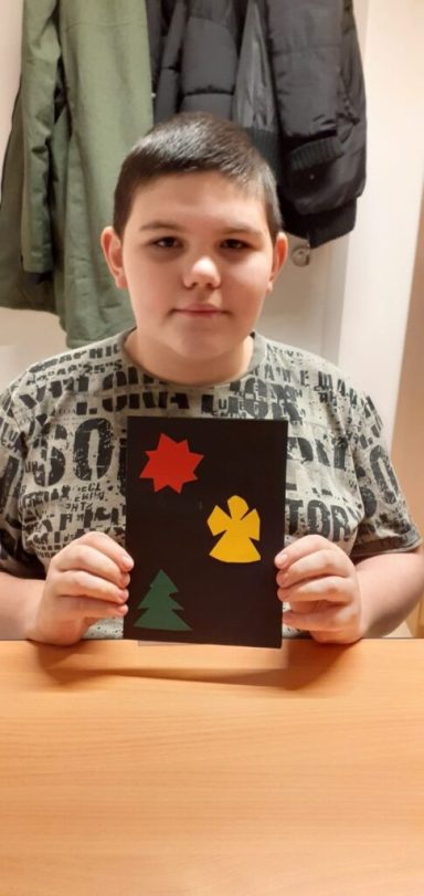 Ein Junge hält ein Kunstwerk mit einem Baum, einer Schneeflocke und einem Engel.