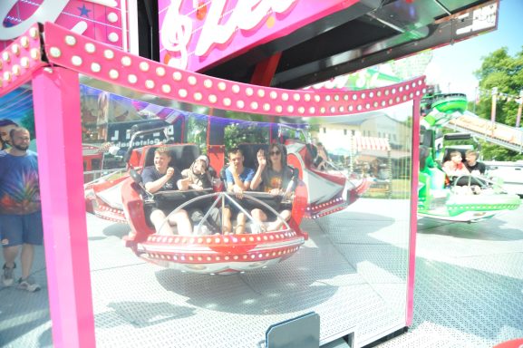 Gruppe von Fahrgästen in einem Fahrgeschäft, umgeben von bunten Attraktionen.