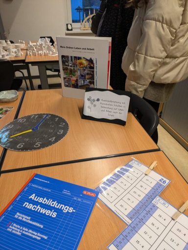 Tisch mit Lernmaterialien, Uhrenmodell und Notizen in einer Unterrichtsumgebung.