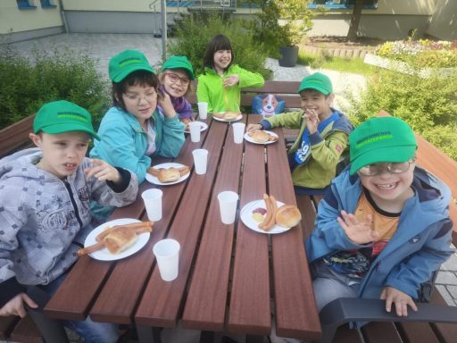 Gruppe von Kindern mit grünen Hüten sitzt an einem Tisch und isst Snacks.
