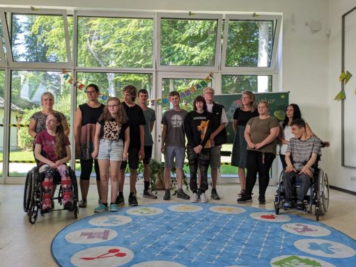 Gruppe von Menschen, darunter Rollstuhlfahrer, in einem Raum mit großen Fenstern.