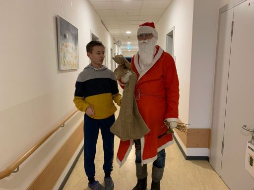 Ein Junge steht neben einem Weihnachtsmann in einem Flur. Beide lächeln.