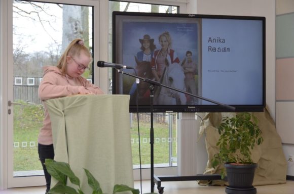 Mädchen spricht am Mikrofon vor einer Präsentation mit historischen Figuren.
