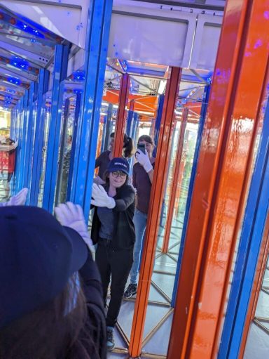 Person mit schwarzer Kleidung in einem bunten Labyrinth aus Stangen.