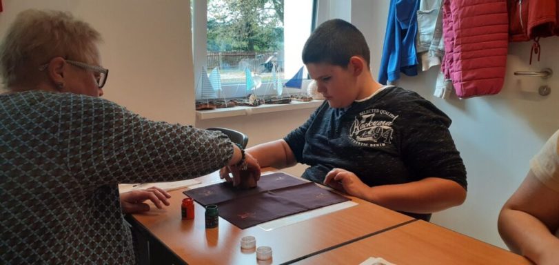 Eine Person hilft einer anderen beim Spielen an einem Tisch in einem hellen Raum.