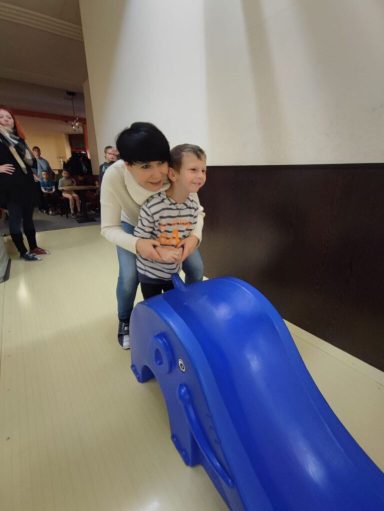 Ein Kind mit einem Erwachsenen auf einer blauen Rutsche in einem Innenraum.