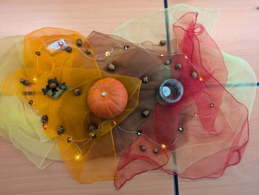 Bunte Dekoration mit Tuch, einer kleinen Kürbis und Eicheln auf einem Tisch.