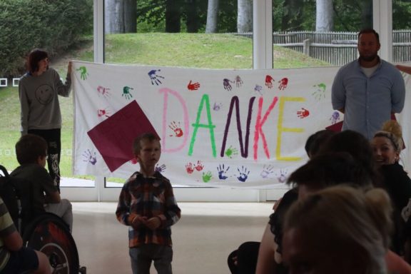 Banner mit buntem Schriftzug „DANKE“ und Kindern im Vordergrund.