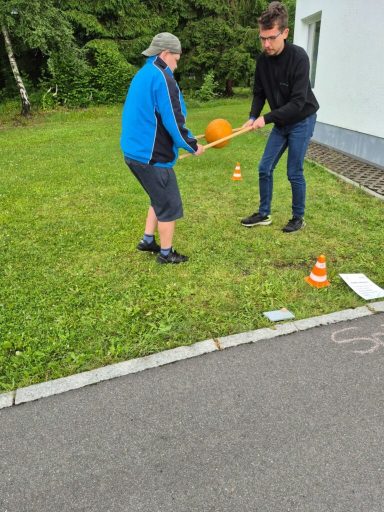 Zwei Personen spielen im Freien mit einem orangen Ball und vermeiden kleine Hindernisse.