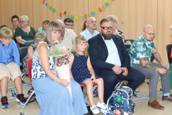 Eine Frau mit Blumenstrauß sitzt neben einem kleinen Mädchen und einem Mann in Anzug.