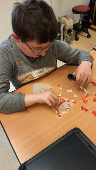 Ein Junge klebt bunte Papierschnipsel auf einen Tisch.