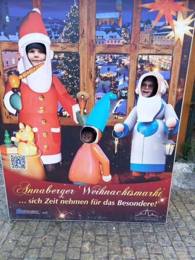 Kinder stecken in Figurenkostümen vor festlicher Hintergrundleinwand.