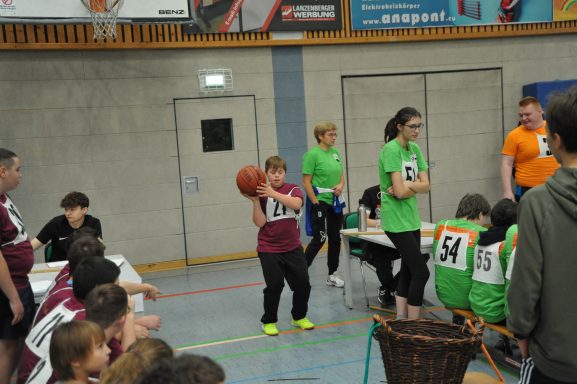 Junge mit Basketball in der Hand, umgeben von anderen Spielern und Betreuern in Sportkleidung.
