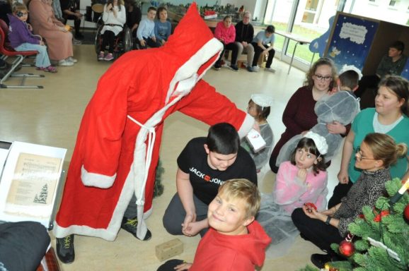 Eine Person im roten Weihnachtsmannkostüm interagiert mit Kindern in festlicher Umgebung.