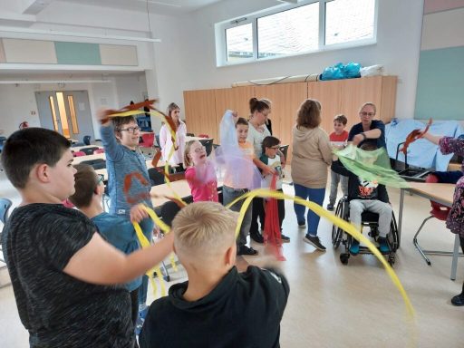 Gruppenaktivität mit Kindern, die bunte Bänder in einem Klassenzimmer halten.