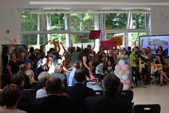 Feierliche Versammlung mit Menschen, die Plakate halten und auf einer Bühne stehen.