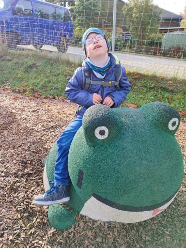 Ein Junge sitzt auf einem grünen Frosch-Spielgerät und blickt nach oben.