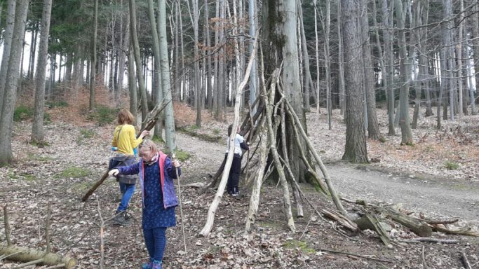 Kinder spielen im Wald und erkunden einen großen Baumstamm.