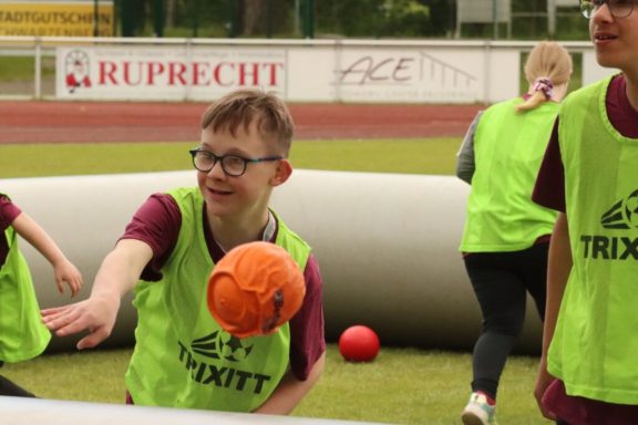Ein Junge mit Brille wirft einen Basketball, umgeben von anderen Kindern in grünen Westen.