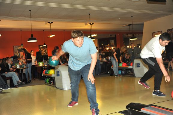 Zwei Jugendliche beim Bowling in einer belebten Bowlingbahn.