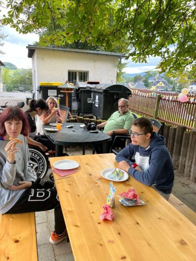 Gruppe von Personen bei einem Treffen im Freien, wartend auf das Essen am Holztisch.
