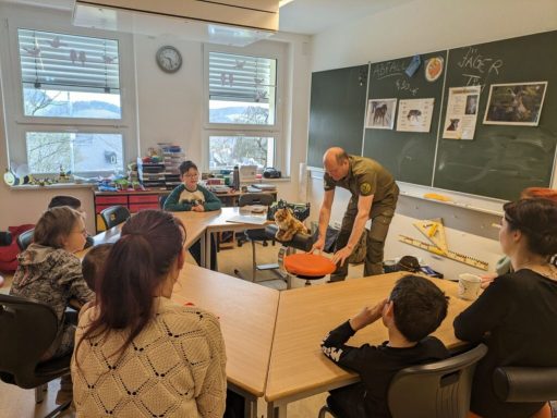 Eine Gruppe von Kindern und Erwachsenen im Klassenzimmer mit einem Hundetrainer.