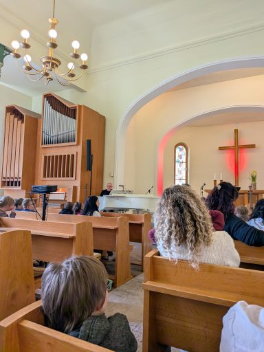 Blick ins Innere einer Kirche mit Sitzbänken und einem Kreuz im Hintergrund.