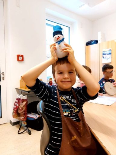 Junge hält einen Schneemann aus Stoff über seinem Kopf und lächelt.