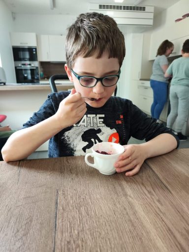 Ein Junge mit Brille isst Joghurt aus einer kleinen weißen Schüssel.